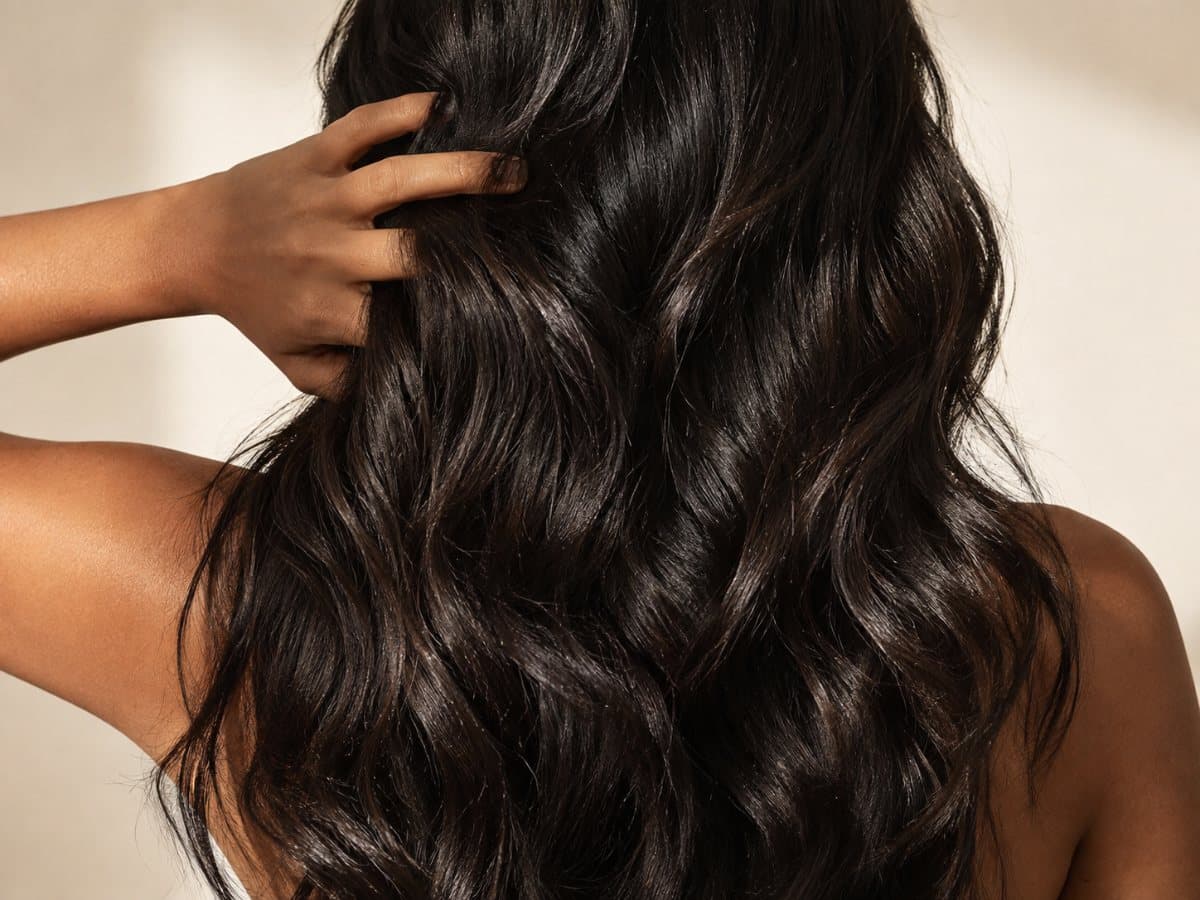 A Sri Lankan woman seen from behind, her long dark hair falling in glossy waves, one hand lifted into it.